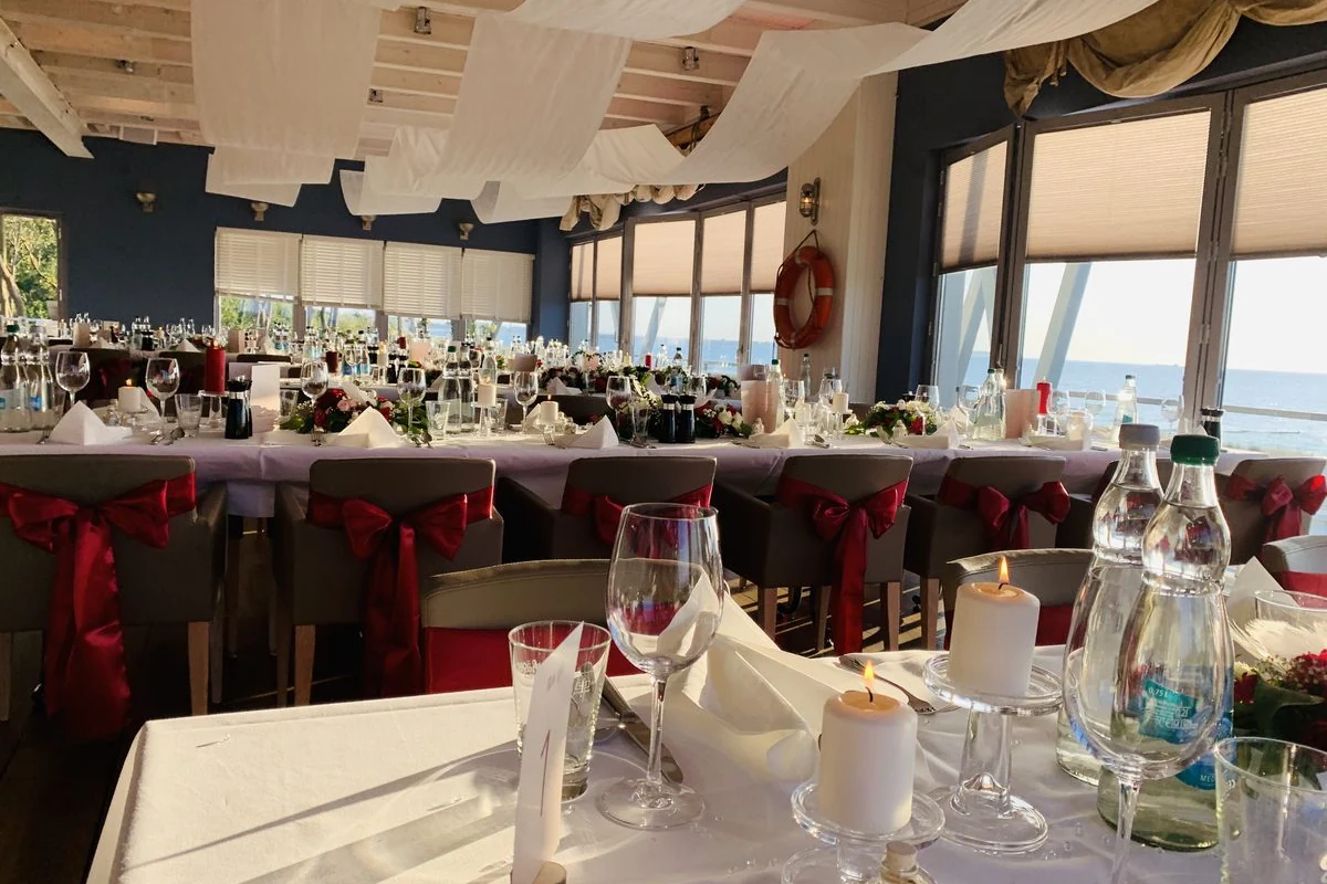 Gedeckter Hochzeitstisch mit Kerzen, Weingl&auml;sern und roten Stuhlschleifen