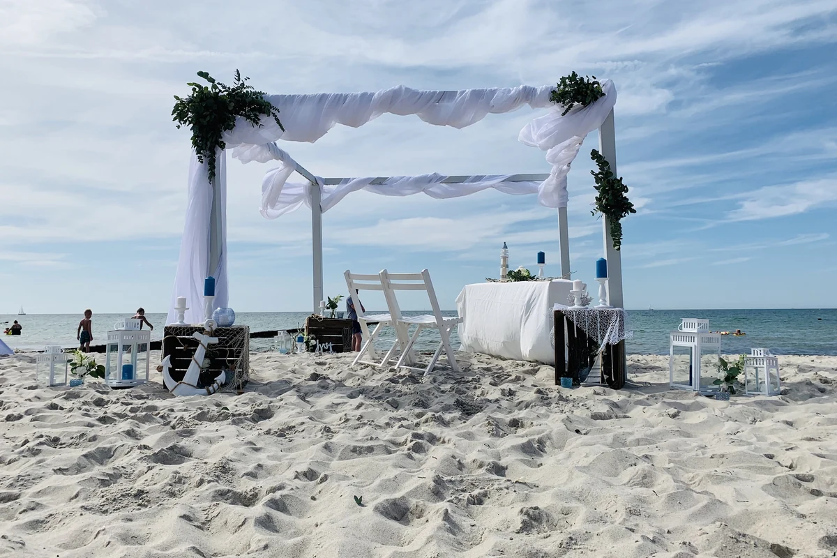 Dekorierter Traupavillon mit wei&szlig;en Tuechern und Gruenschmuck am Strand von Warnem&uuml;nde, dahinter die Ostsee